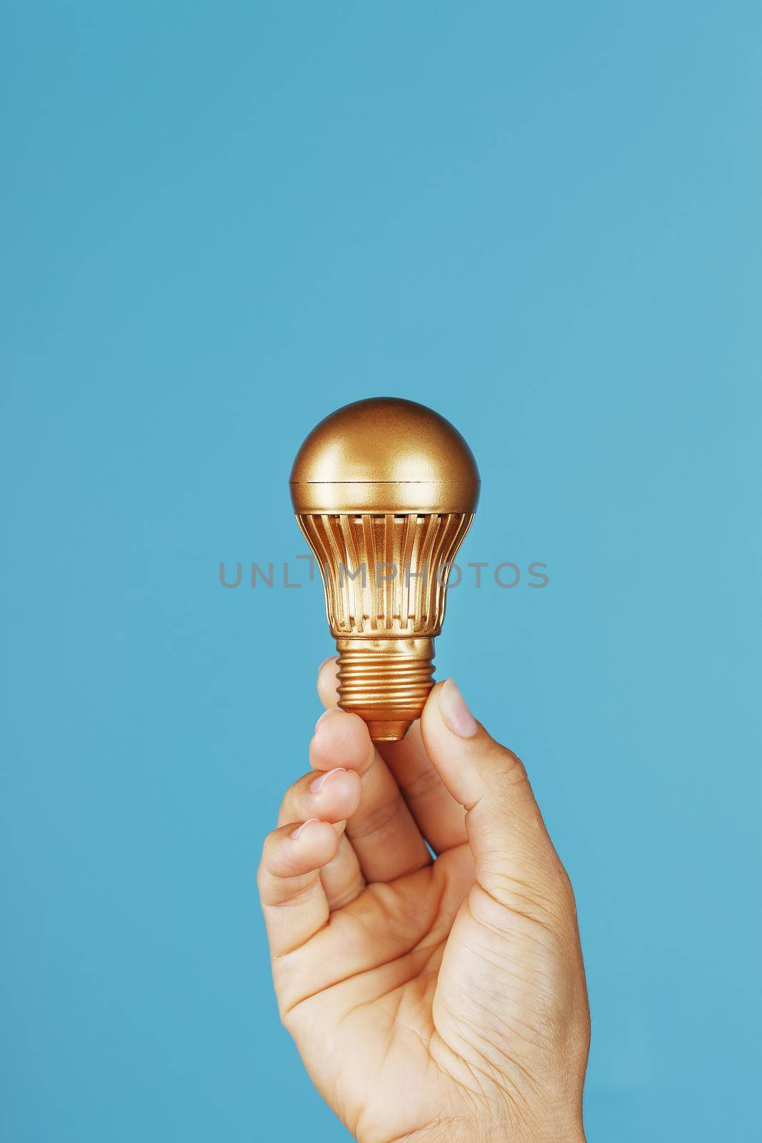 Gold light bulb as an idea in a female hand on a blue background. by AlexGrec