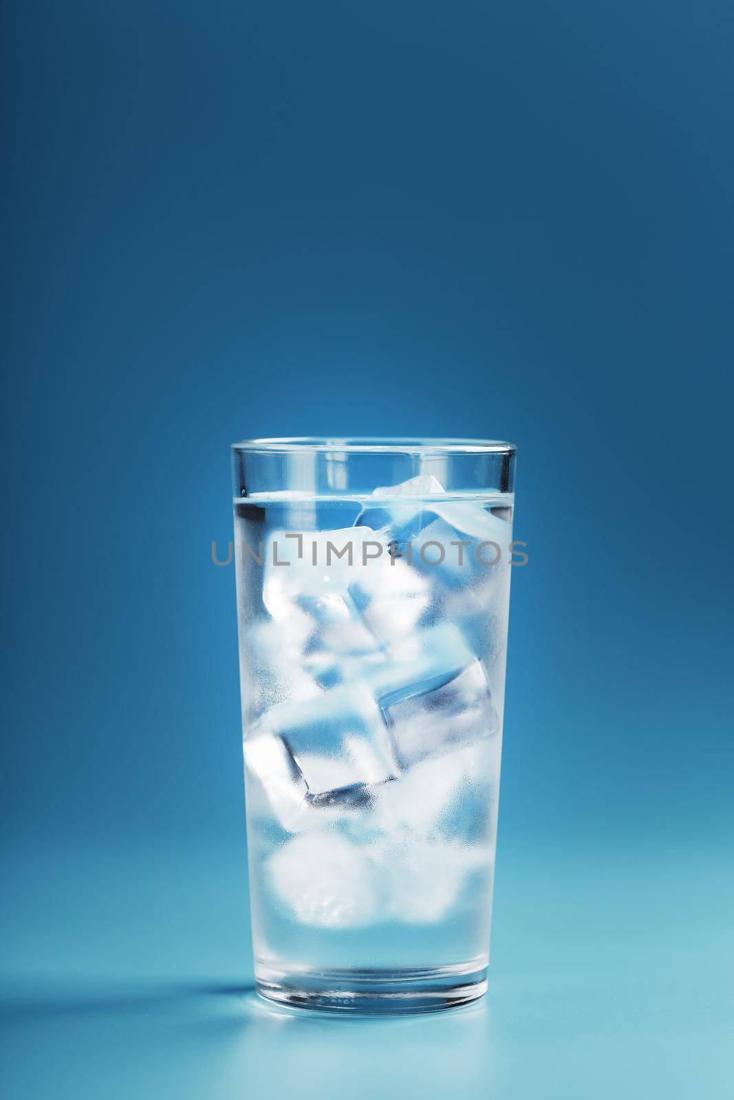 Glass with water and ice cubes on a blue background. Rescue concept on a hot sultry day. Free space