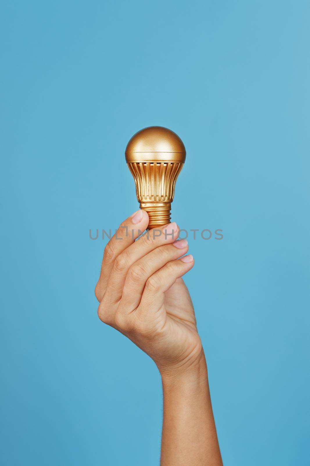Gold light bulb as an idea in a female hand on a blue background.