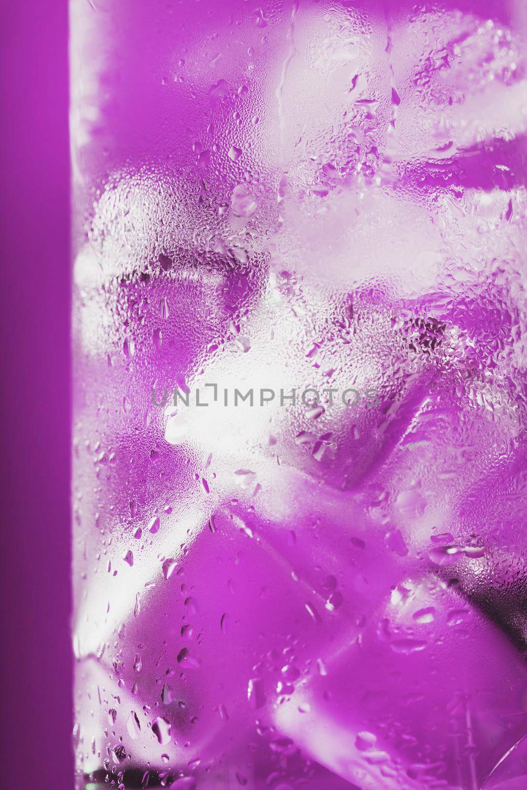Ice cubes in a glass with refreshing ice water on a pink background. Close-up