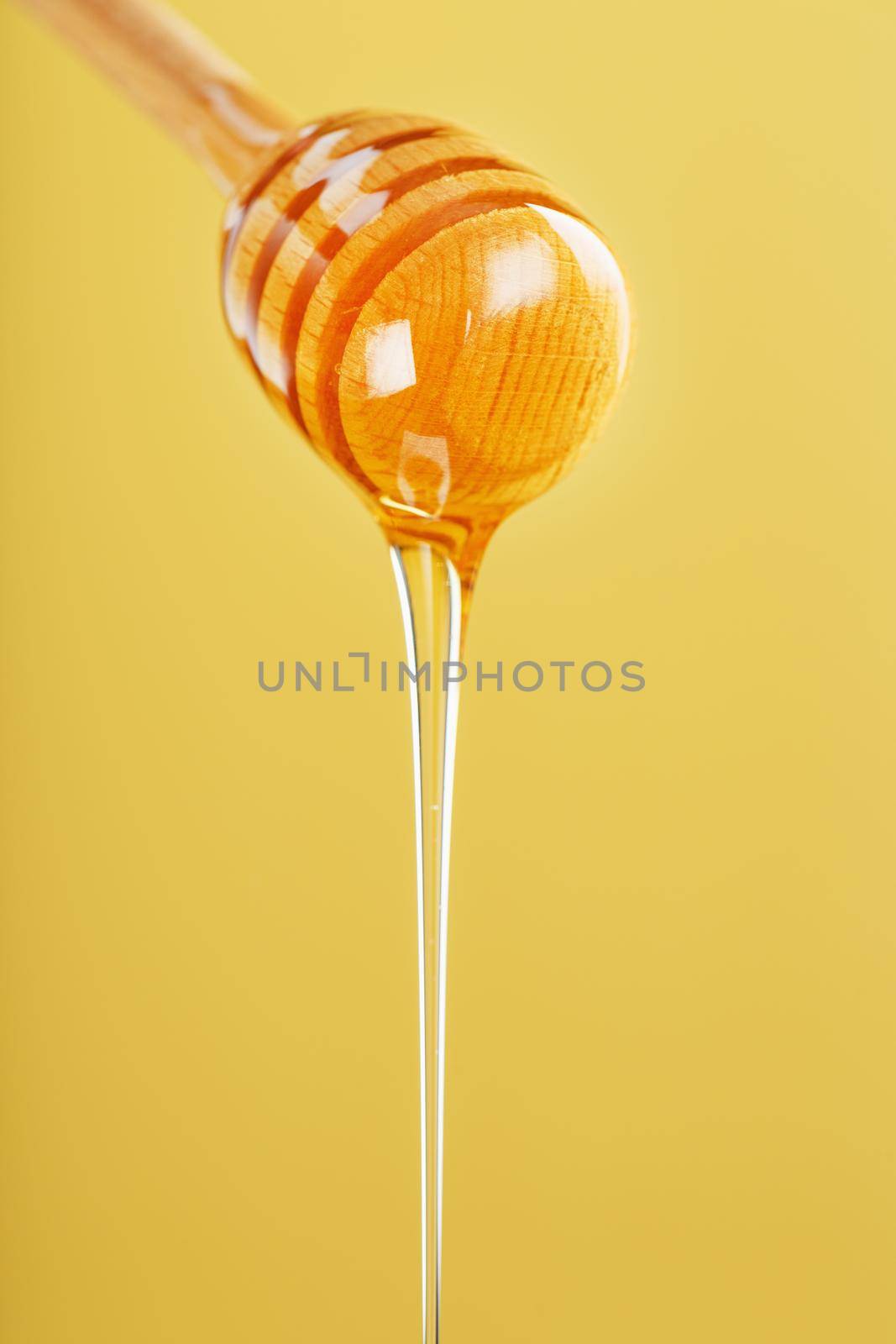 Golden honey trickles from a wooden honey dipper on a yellow background. Healthy food diet concept, ecologically pure product