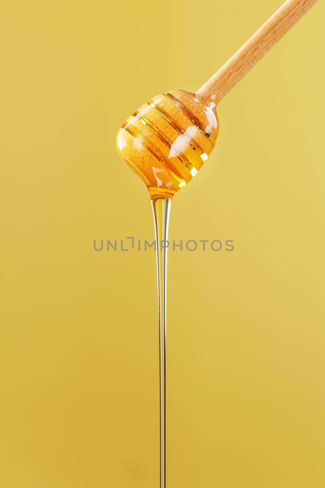 Golden honey trickles from a wooden honey dipper on a yellow background