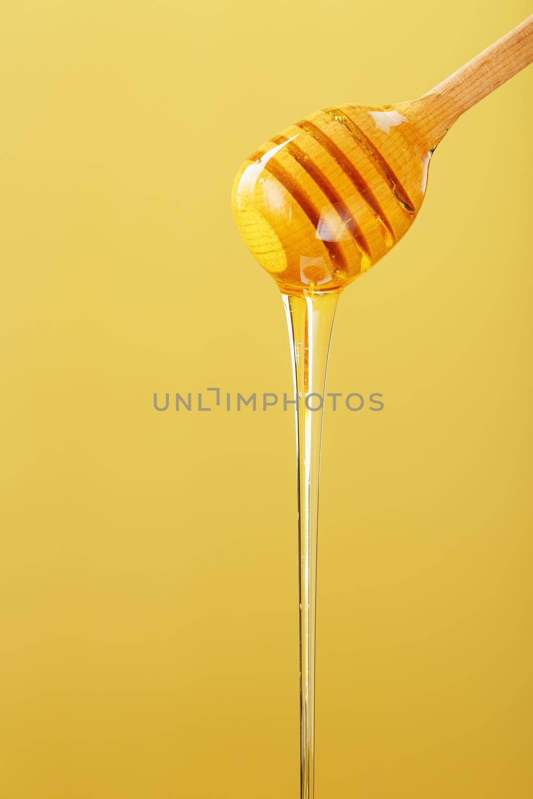 Golden honey trickles from a wooden honey dipper on a yellow background. Healthy food diet concept, ecologically pure product