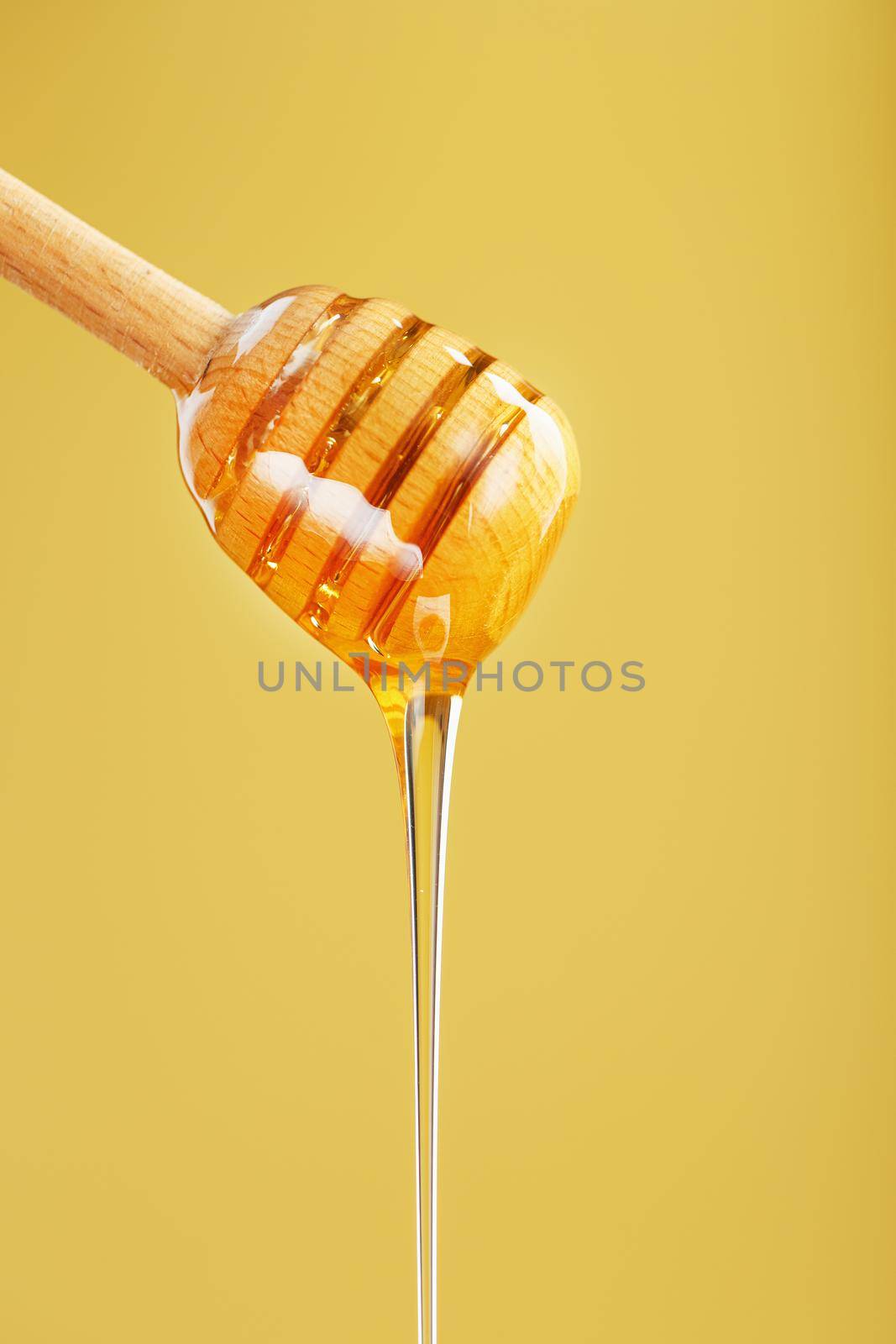 Honey flows down from a honey bucket on a yellow background. The concept of healthy and eco-friendly nutrition