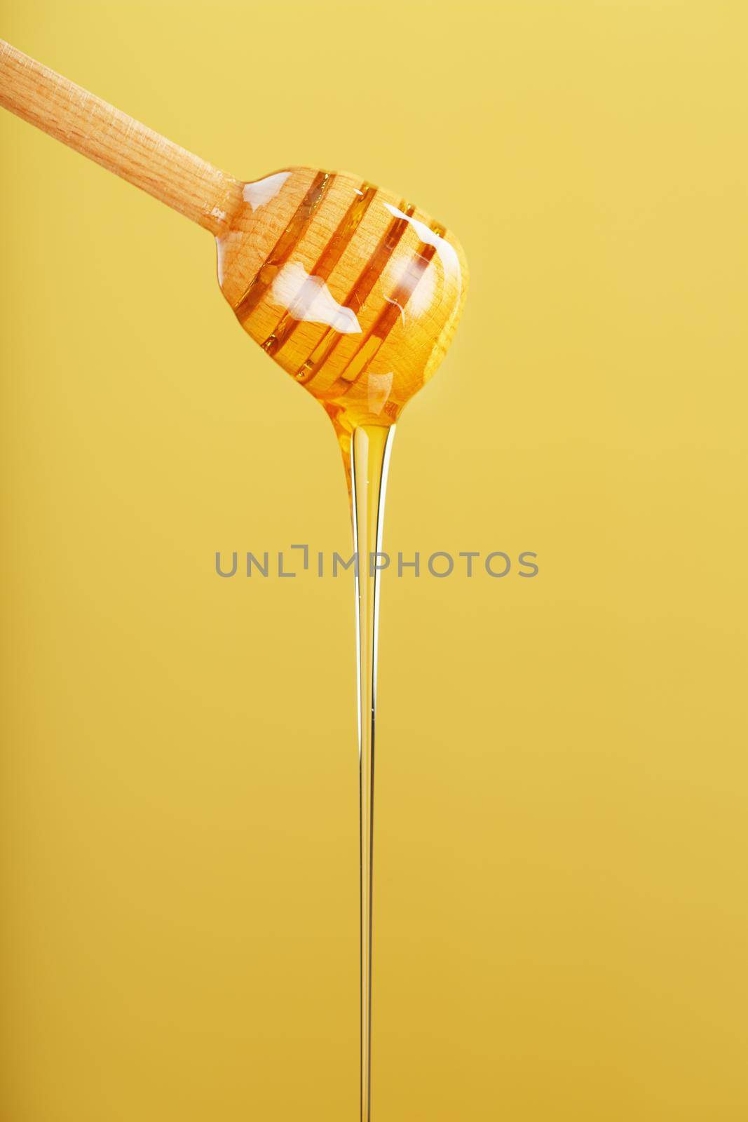 Honey drips in a thin stream from a honey dipper on a yellow background. by AlexGrec