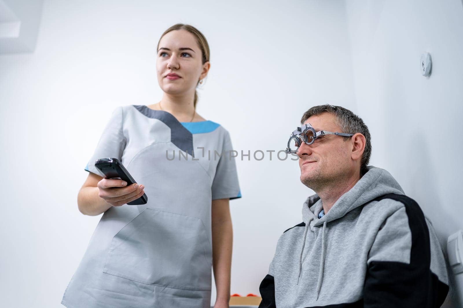 Vision correction. Selection of eyeglasses. Professional trial frames on male patient face while doctor checks eyesight in modern ophthalmologist office. Optometrist checking prescription for glasses by Tomashevska