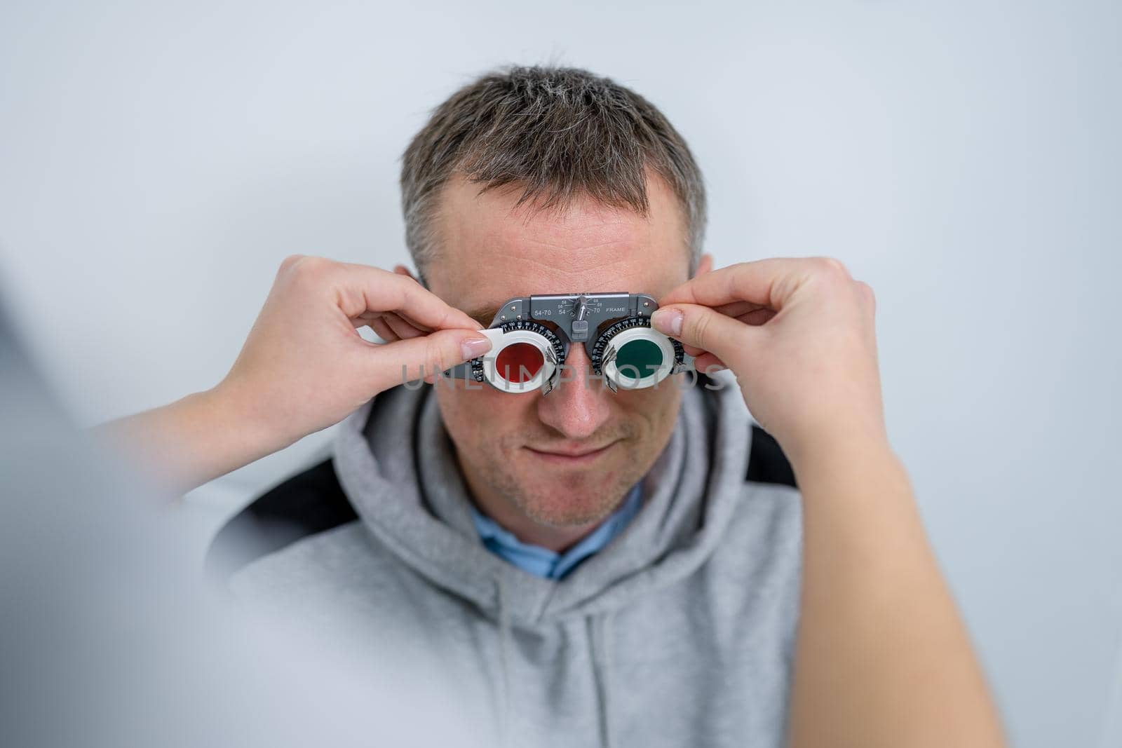 Male patient undergoes an eye test and prescription for eyeglasses in ophthalmology clinic. Optometrist checking patient eyesight and vision correction. Changing lenses on trial frame on patient nose.