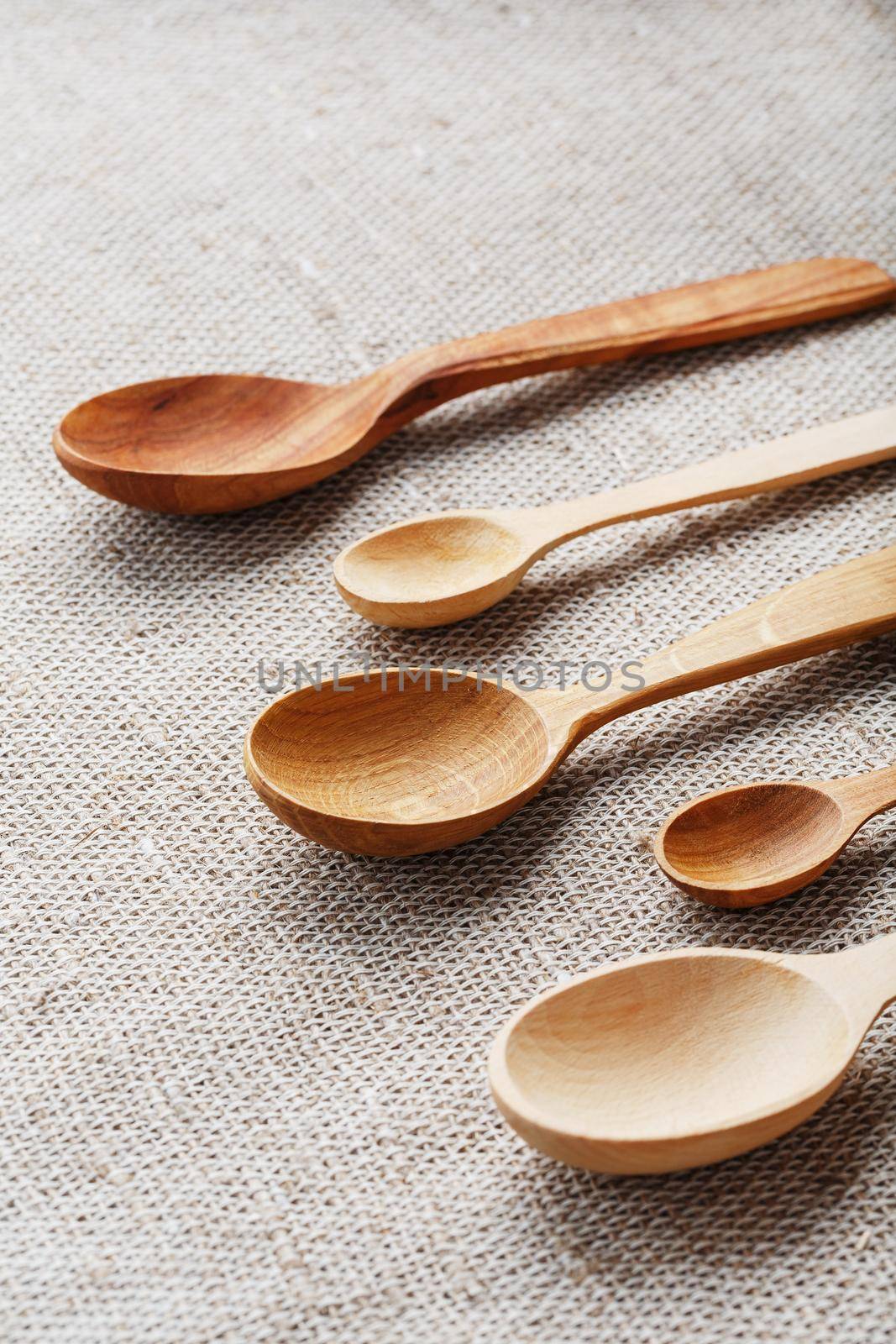 Craft spoons made from different types of wood lie in a row on a hemp burlap fabric