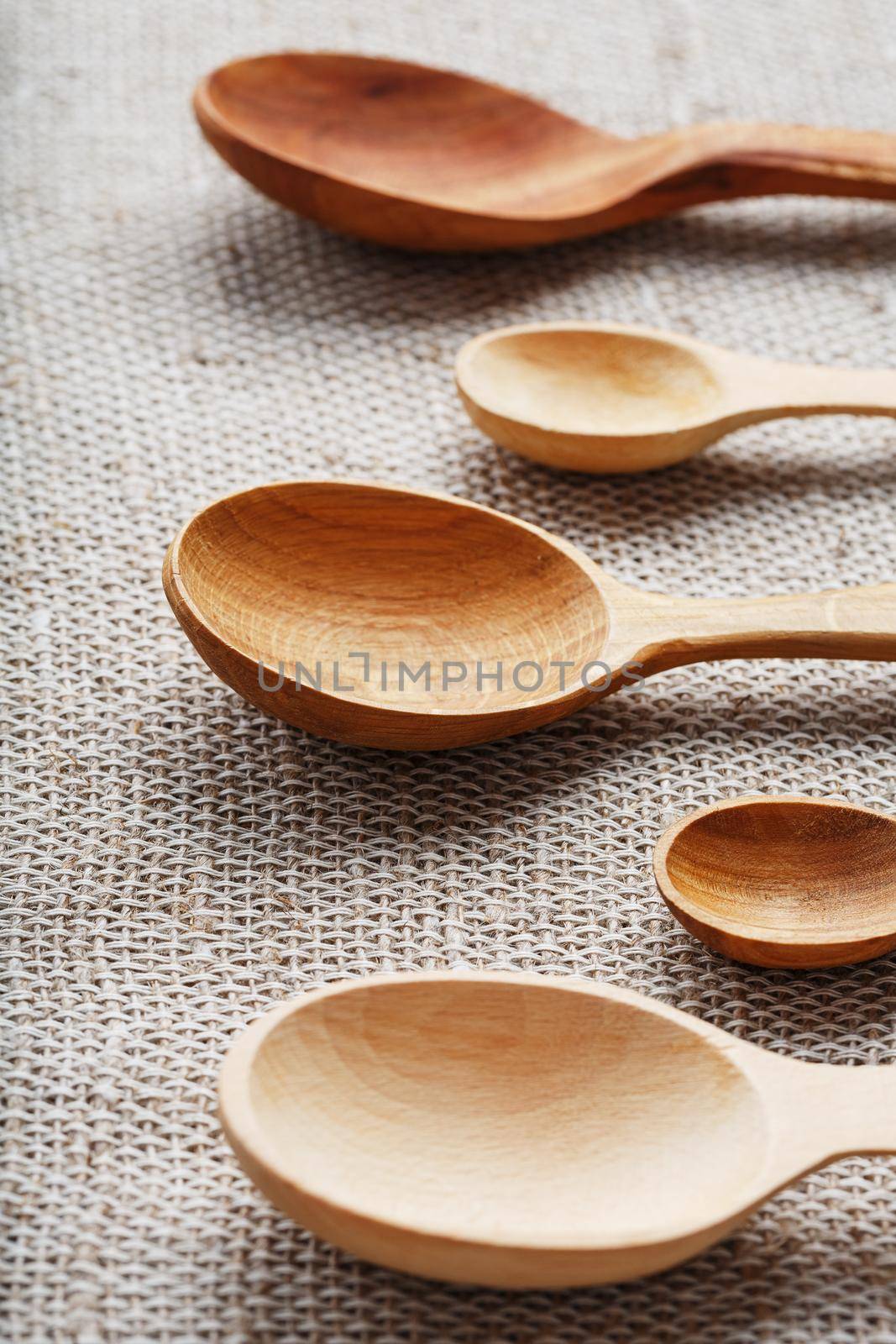 Craft spoons made from different types of wood lie in a row on a hemp burlap fabric. Top view, free space by AlexGrec