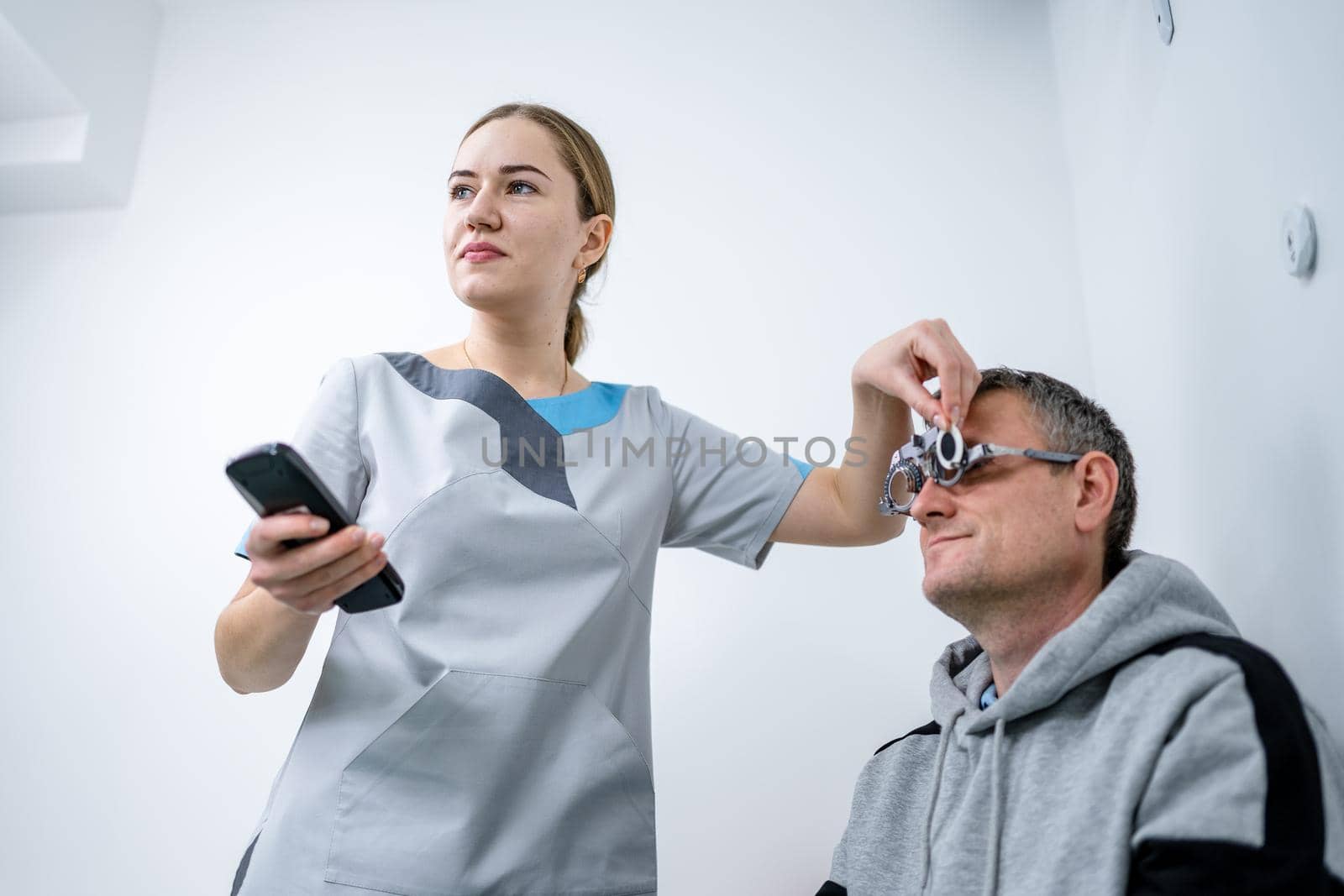 Vision correction. Selection of eyeglasses. Professional trial frames on male patient face while doctor checks eyesight in modern ophthalmologist office. Optometrist checking prescription for glasses.