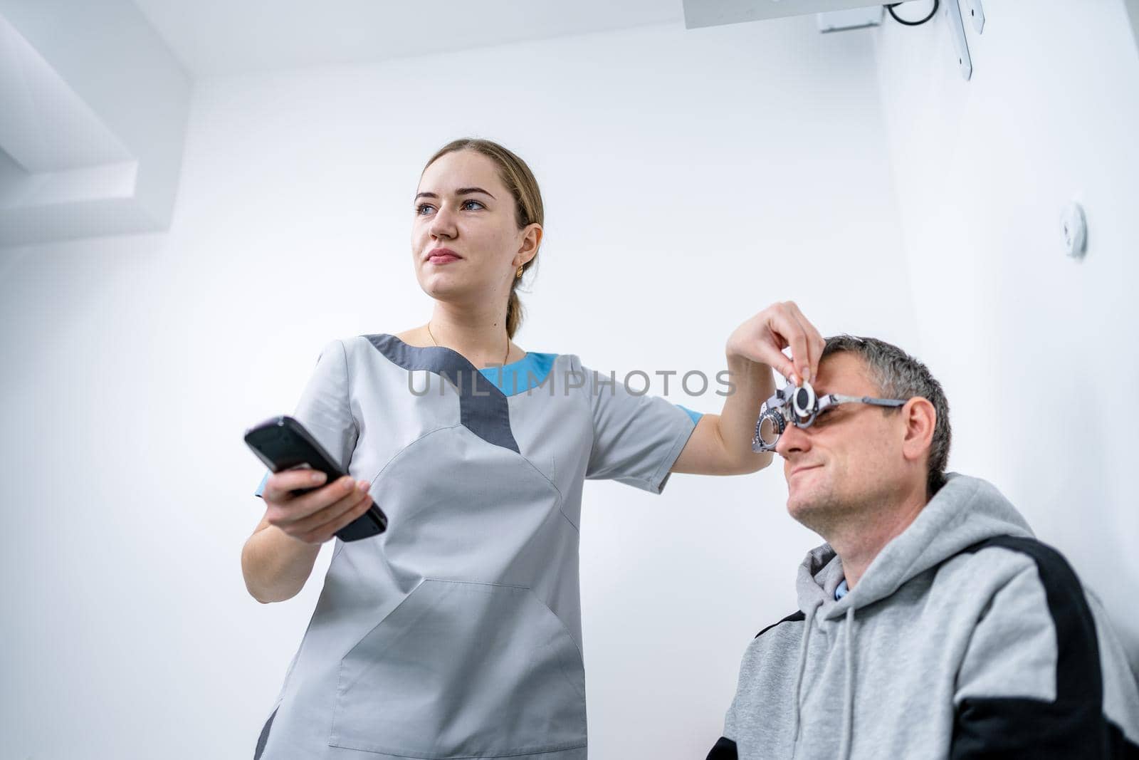 Male patient undergoes an eye test and prescription for eyeglasses in ophthalmology clinic. Optometrist checking patient eyesight and vision correction. Changing lenses on trial frame on patient nose by Tomashevska