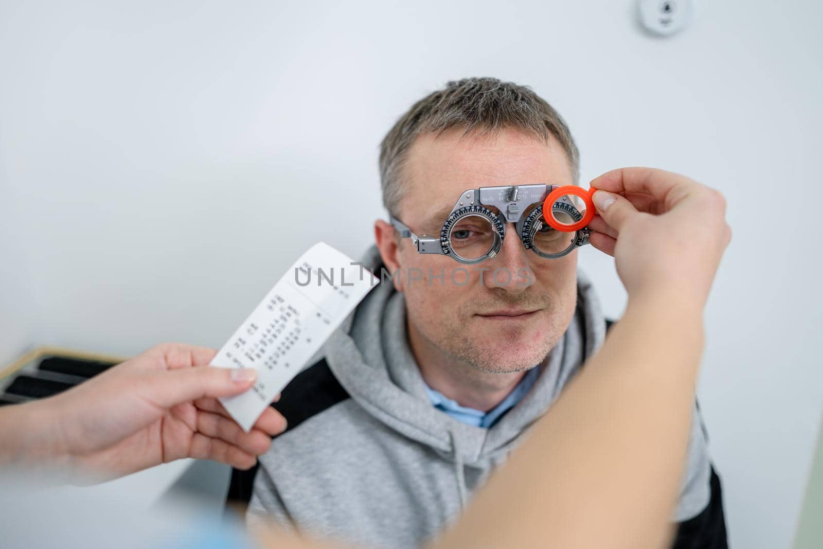 Vision correction. Selection of eyeglasses. Professional trial frames on male patient face while doctor checks eyesight in modern ophthalmologist office. Optometrist checking prescription for glasses by Tomashevska