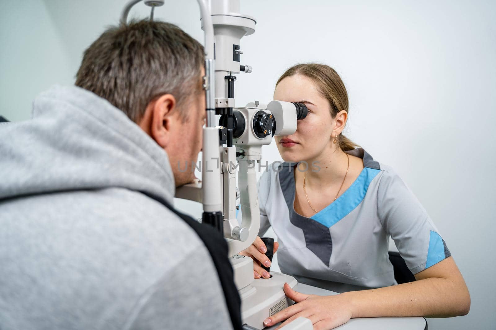 Doctor and patient in ophthalmology clinic. Male patient checking vision with special eye equipment. Optometry concept. Man visiting optician. Patient at slit lamp of optician or optometrist by Tomashevska