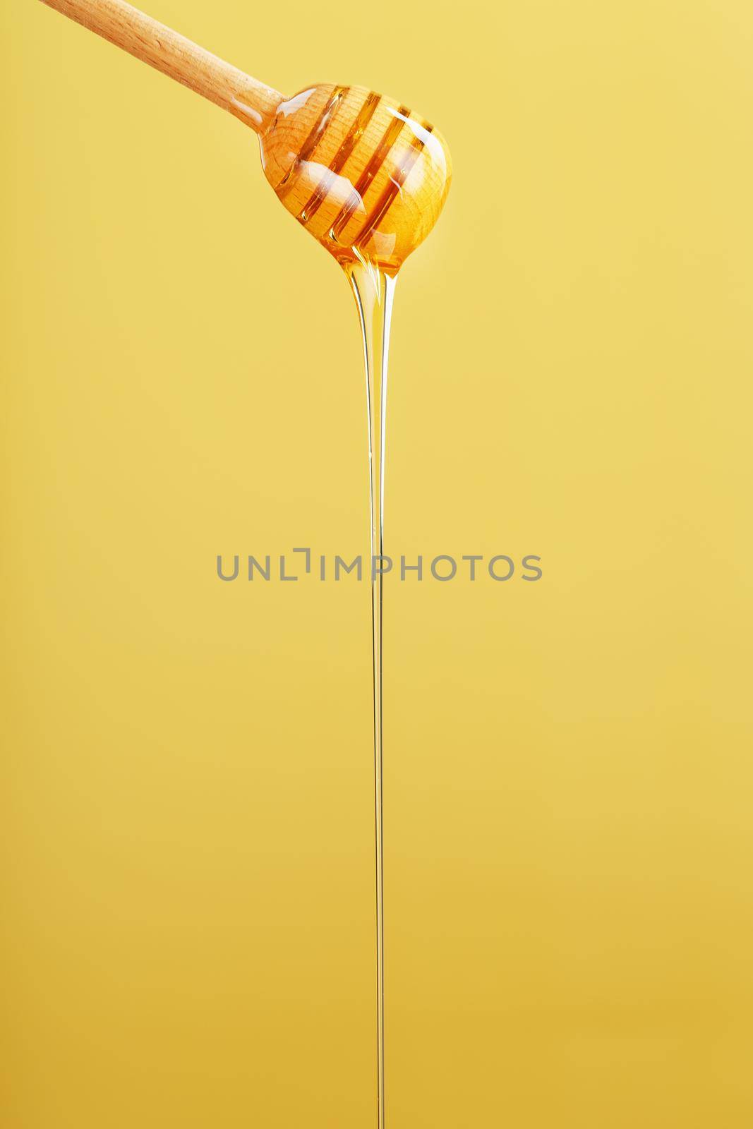 Honey drips in a thin stream from a honey dipper on a yellow background. by AlexGrec