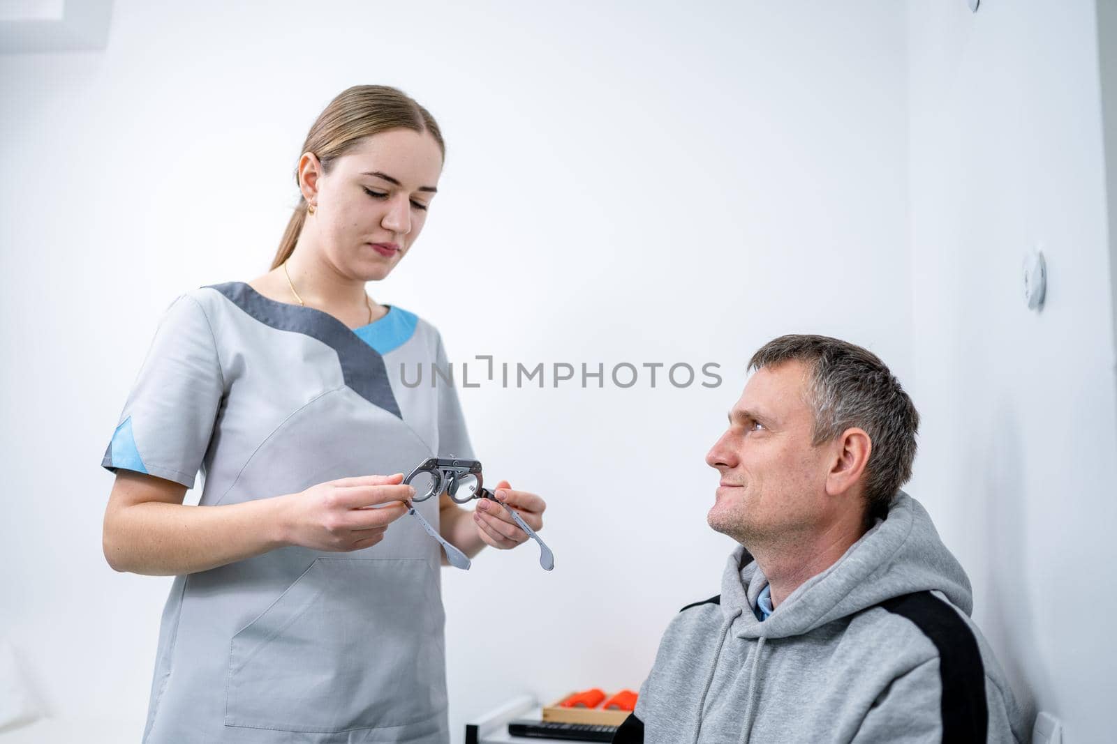 Vision correction. Selection of eyeglasses. Professional trial frames on male patient face while doctor checks eyesight in modern ophthalmologist office. Optometrist checking prescription for glasses.