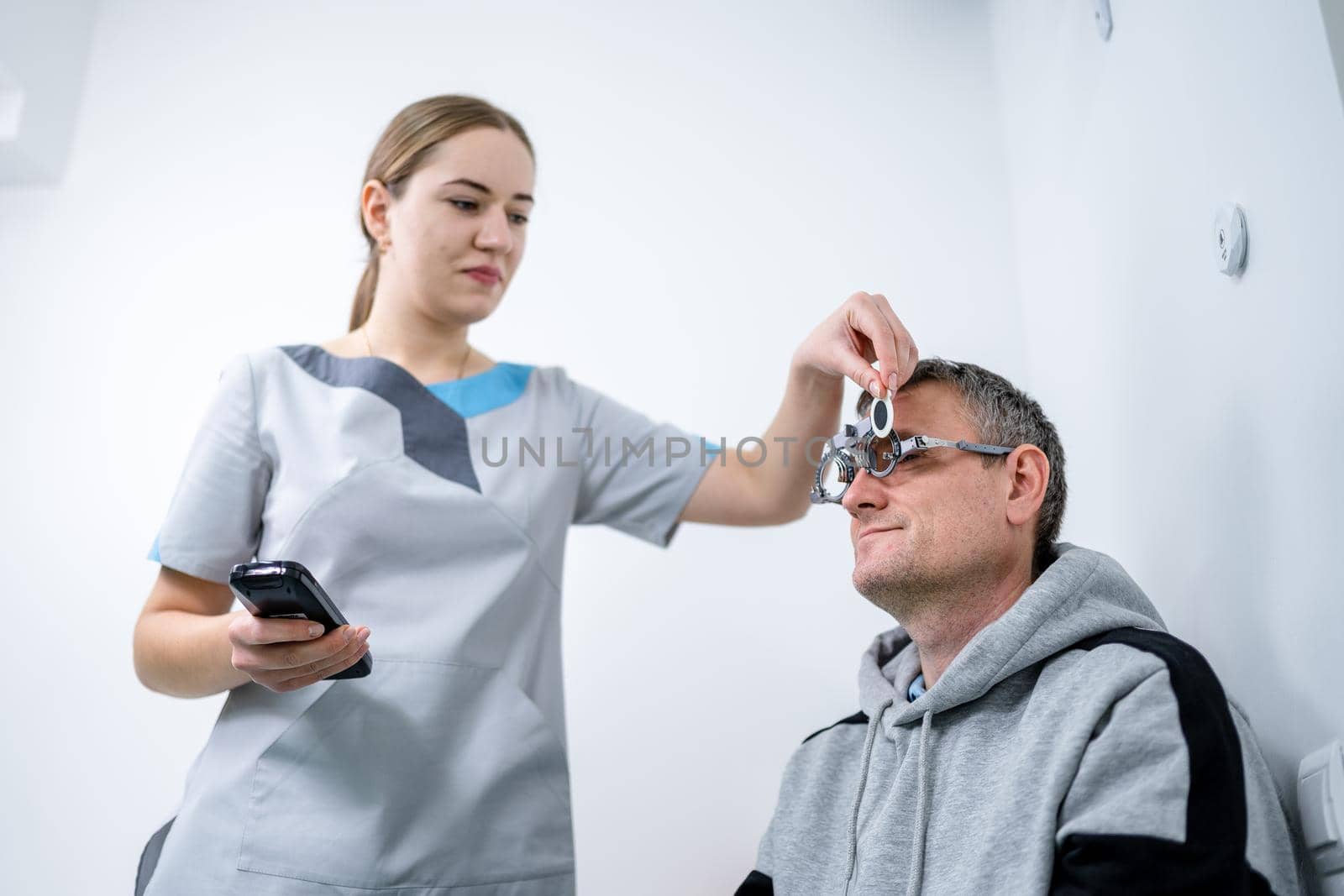 Male patient undergoes an eye test and prescription for eyeglasses in ophthalmology clinic. Optometrist checking patient eyesight and vision correction. Changing lenses on trial frame on patient nose.