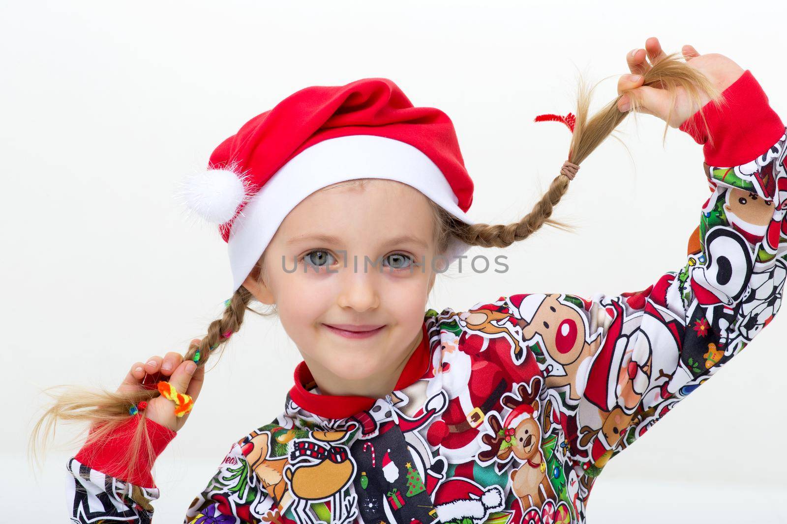 Close up portrait of happy girl with pigtails. Cute joyful girl in bright colorful clothes and Santa Claus cap posing against isolated white background. New Year and Merry Xmas concept