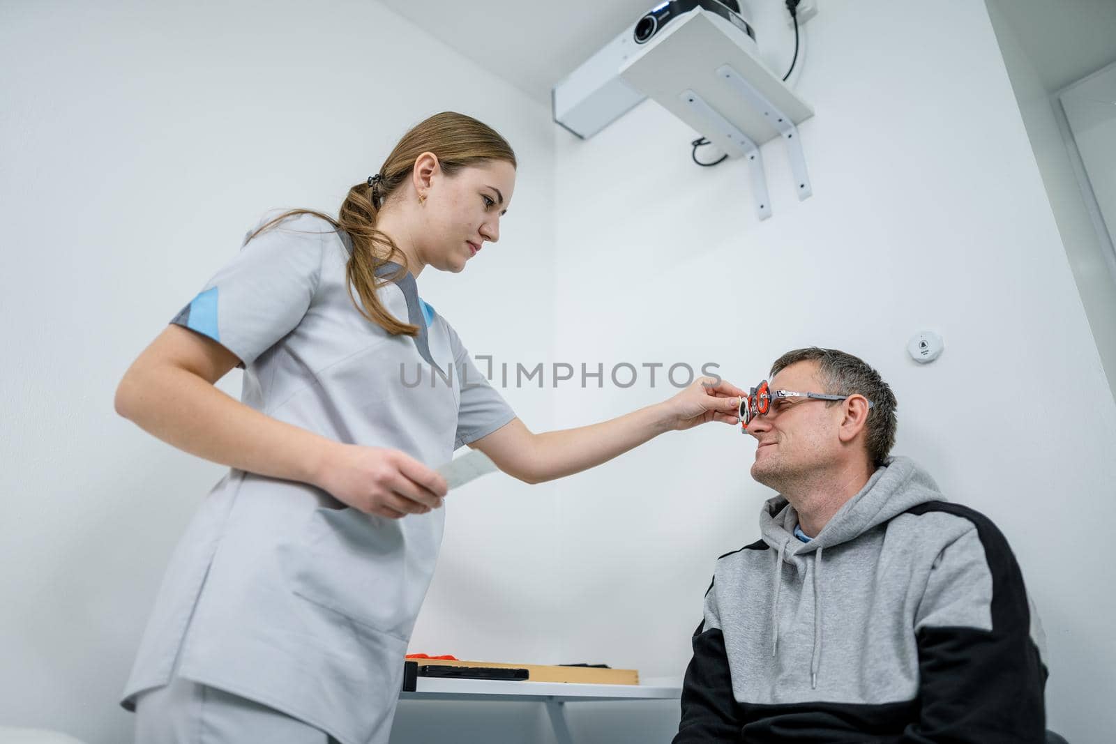 Male patient undergoes an eye test and prescription for eyeglasses in ophthalmology clinic. Optometrist checking patient eyesight and vision correction. Changing lenses on trial frame on patient nose.