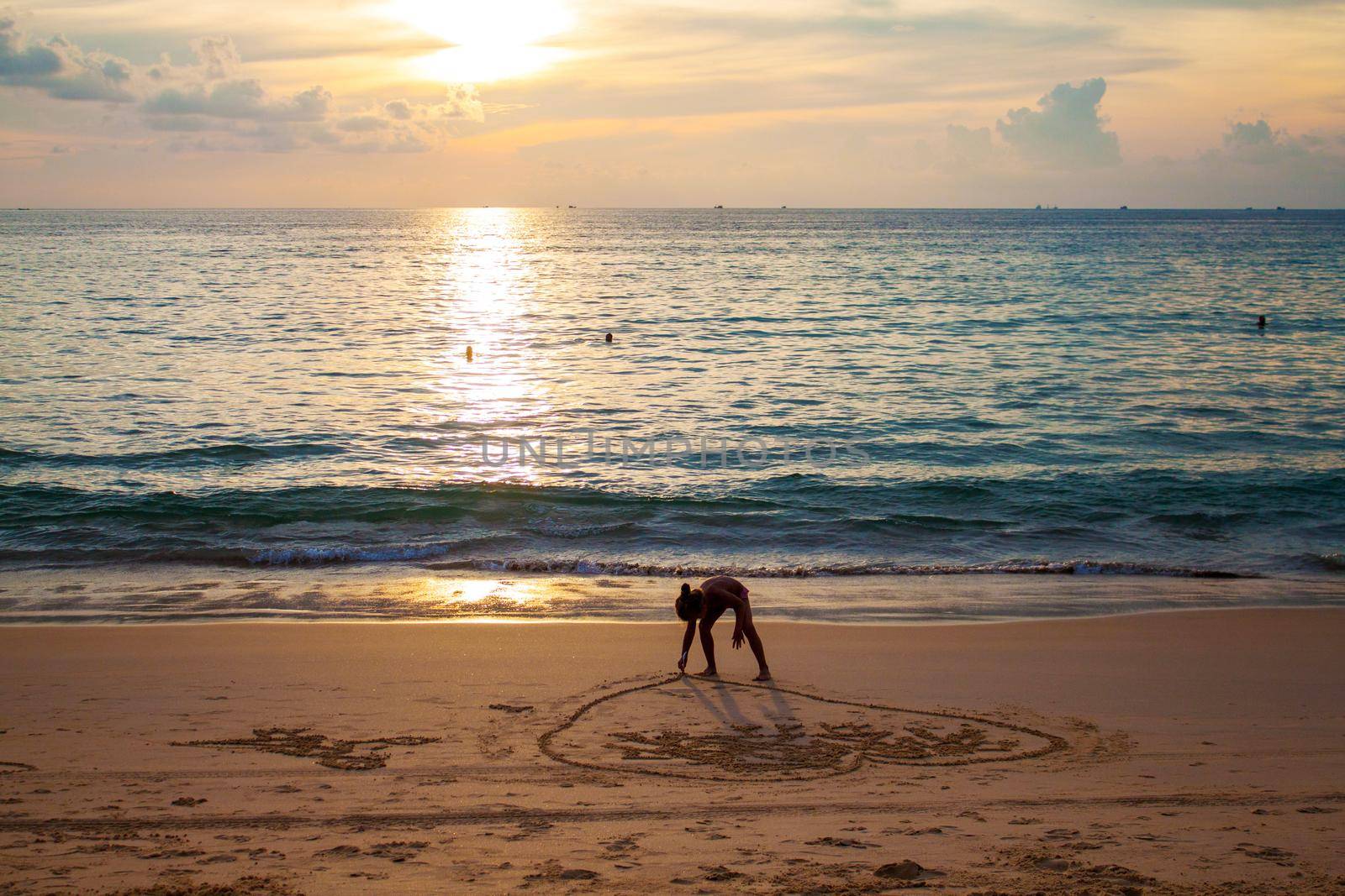 girl painting heart on sand on beach near the sea in sunset by dreamloud