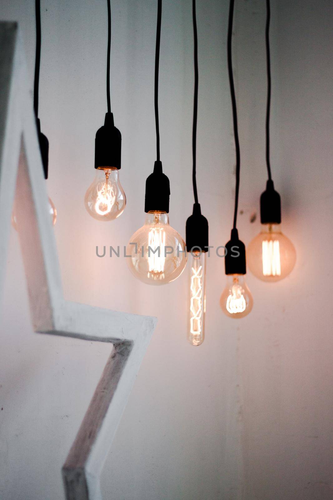 Hanging edison light bulbs on black strings on white wall background by dreamloud