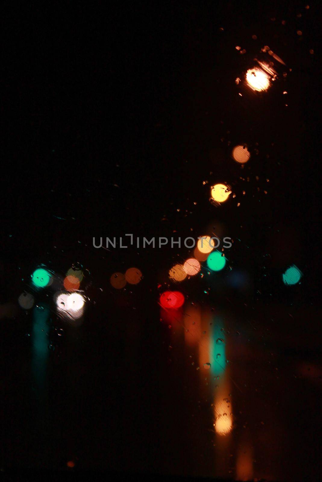 Car traffic lights bokeh through rainy window glass on black background. Defocused city night colorful round lights.  by dreamloud