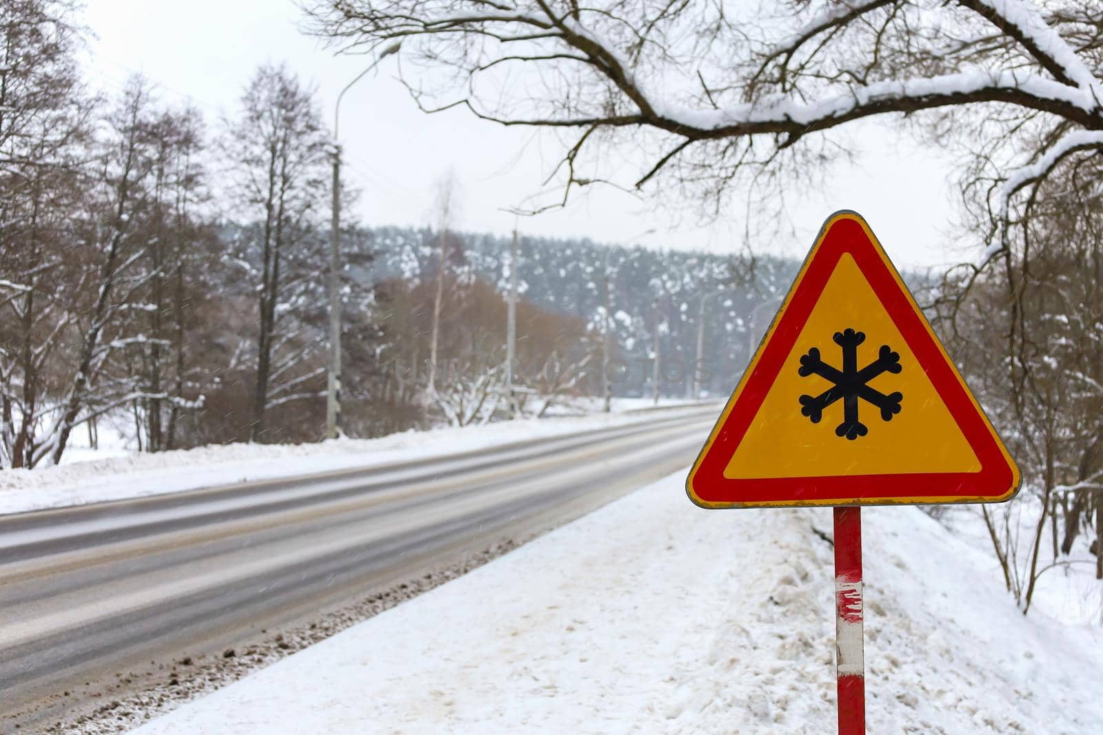 Winter traffic warning sign shows danger of ice and snow at street, highway or road. Winter driving. Temporary road signs on the road. Risk of snow and ice.