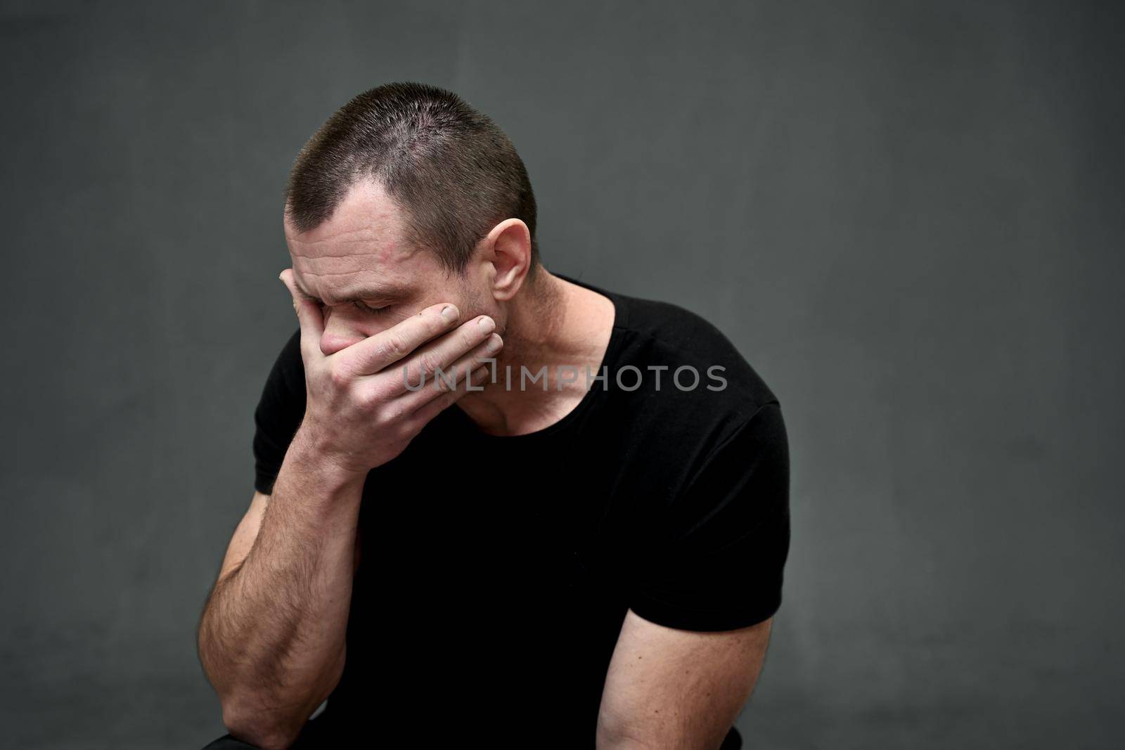 Portrait of an adult caucasian man covered his mouth with his hand on a gray background. Side view