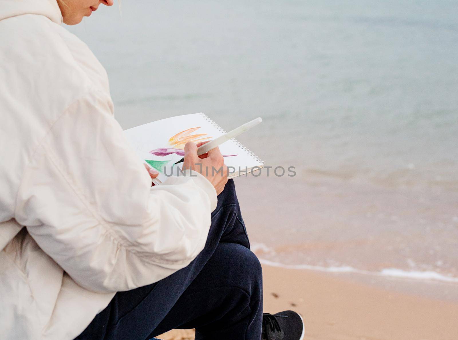 young woman artist painting or doing travel sketches using watercolor by the seaside by Desperada
