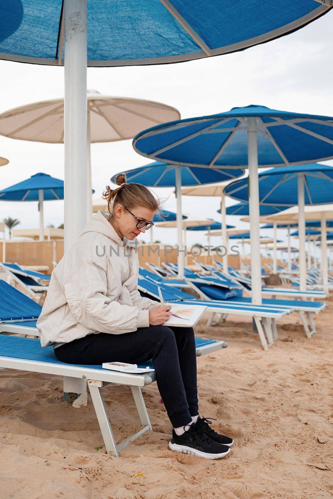 Hobbbies and leisure. young woman artist painting or doing travel sketches using watercolor sitting on the beach