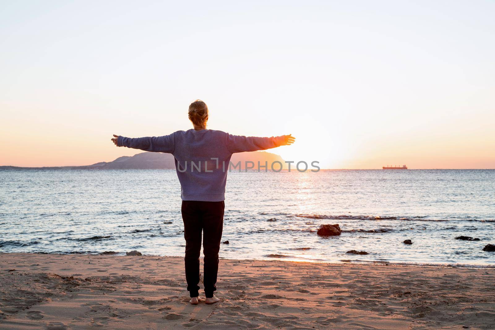 Health and wellness. Young woman in sport clothes enjoying sunrise standing at the beach, doing workout