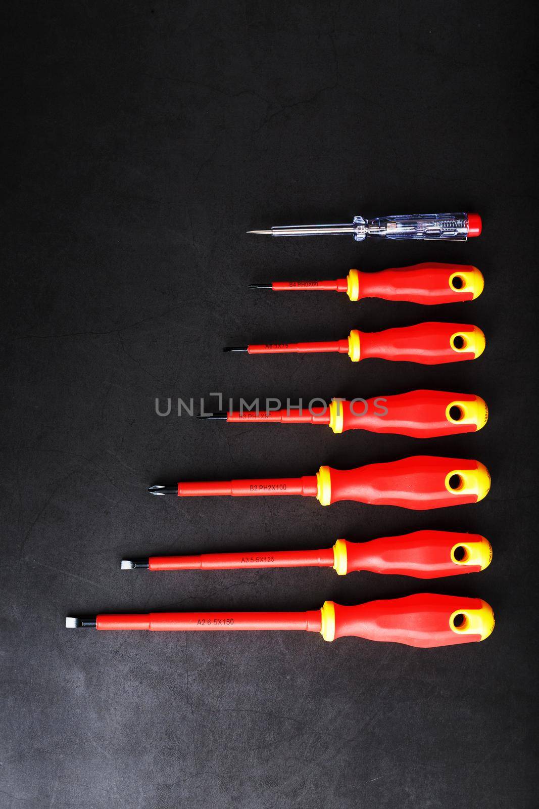 A set of red screwdrivers in a row on a black background. by AlexGrec