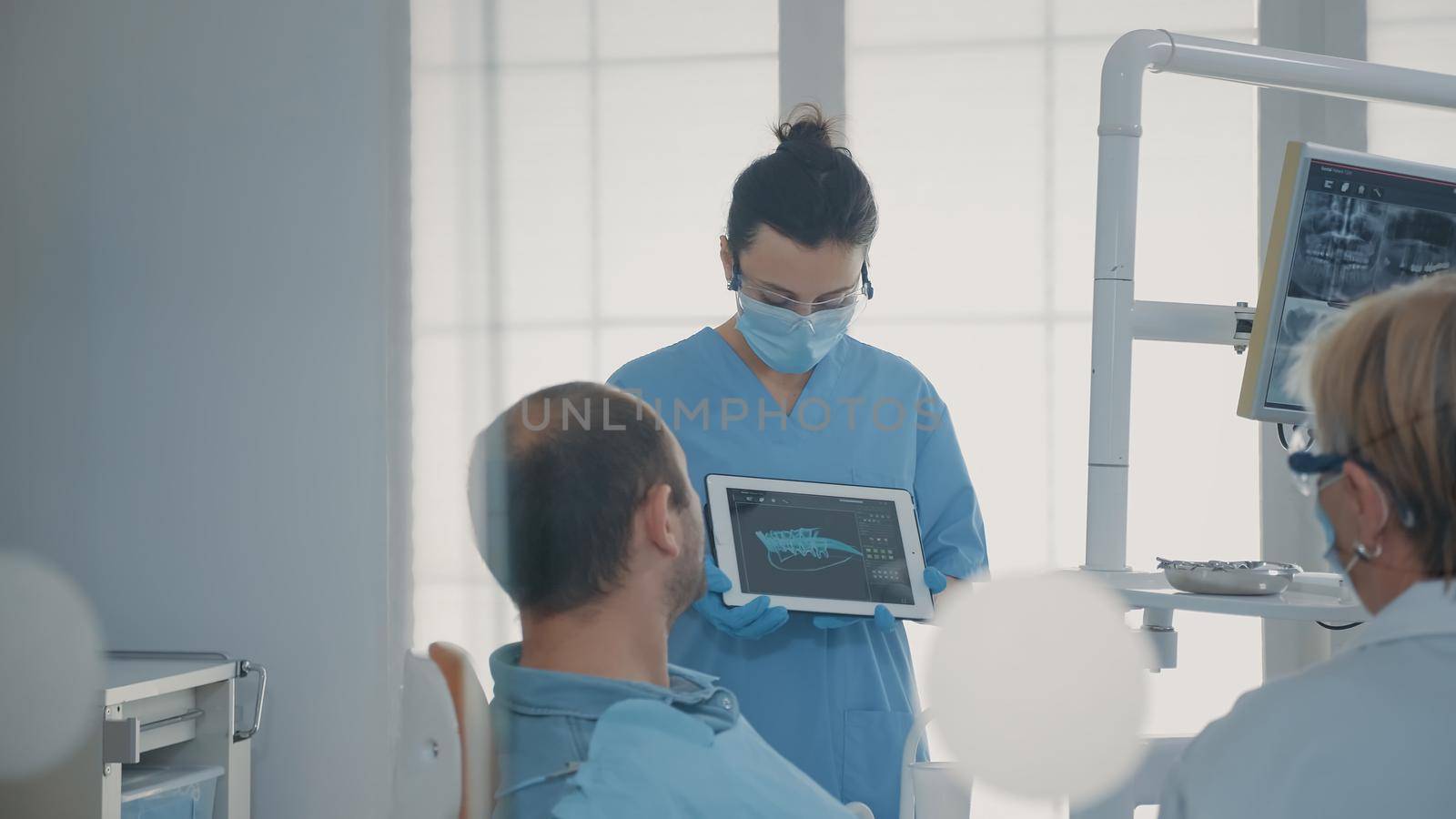 Orthodontic nurse holding x ray results on tablet to show and explain diagnosis to patient in dentistry office. Team of experts showing teeth radiography on device, talking about implant.