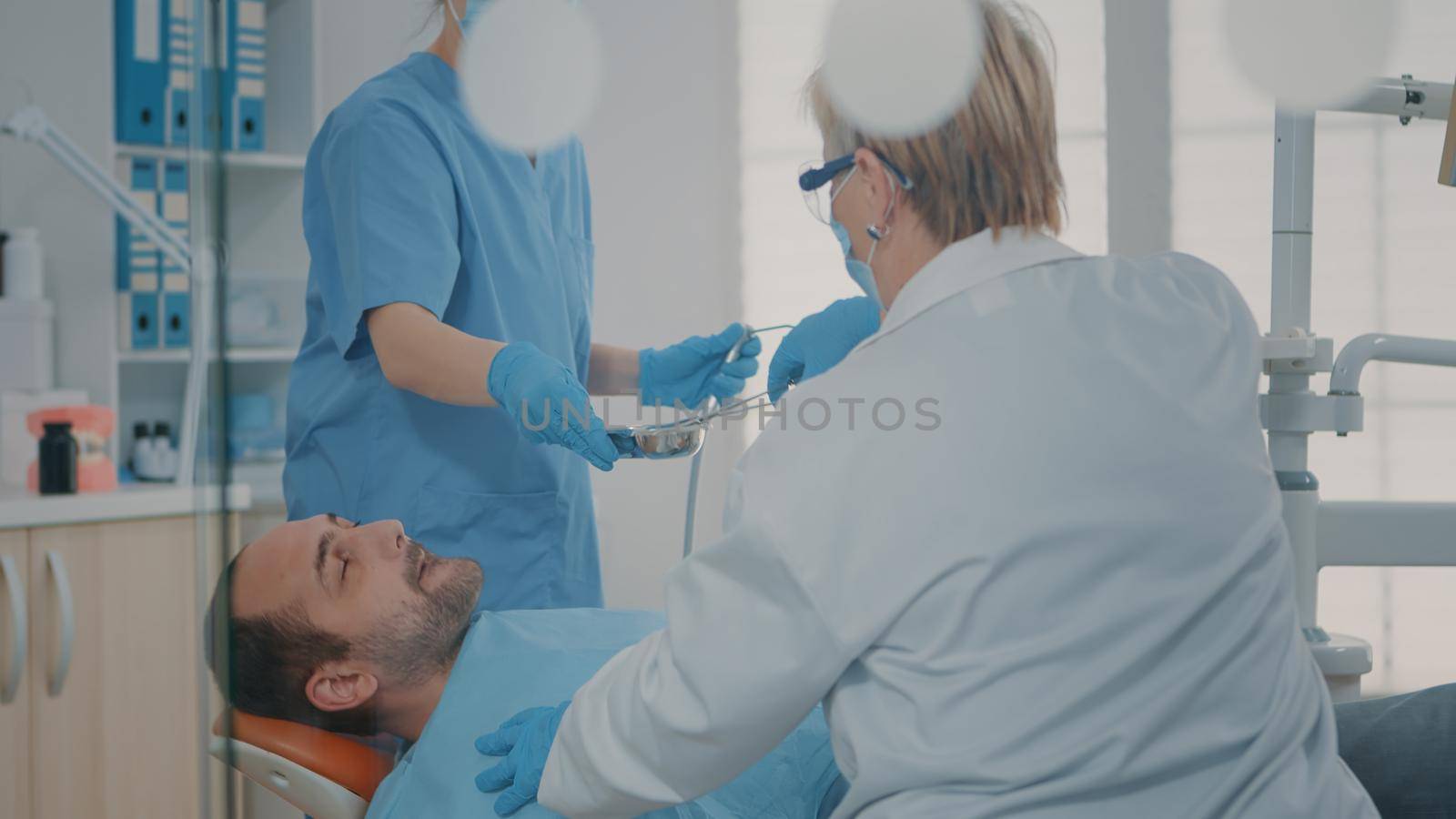 Team of specialists doing surgical procedure on man with toothache, using dental tools and instrument for stomatology operation. Dentist and nurse extracting teeth at oral care clinic.