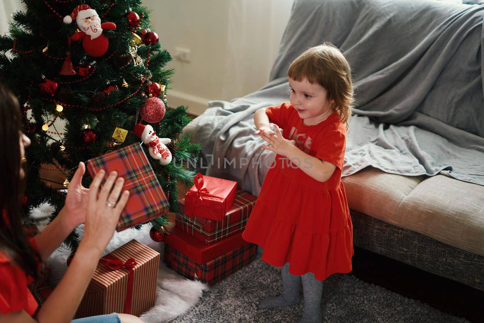 Caucasian girl and mom in red clothes decorating fir tree on Christmas holidays