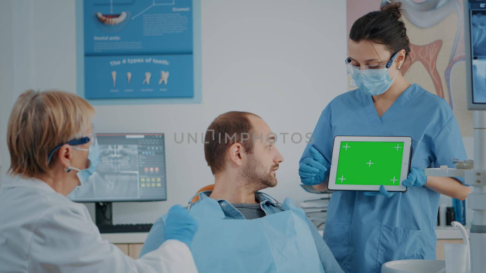 Patient and dentistry team looking at tablet with green screen. People in stomatology cabinet using isolated template with mockup copy space and chroma key background on digital device.