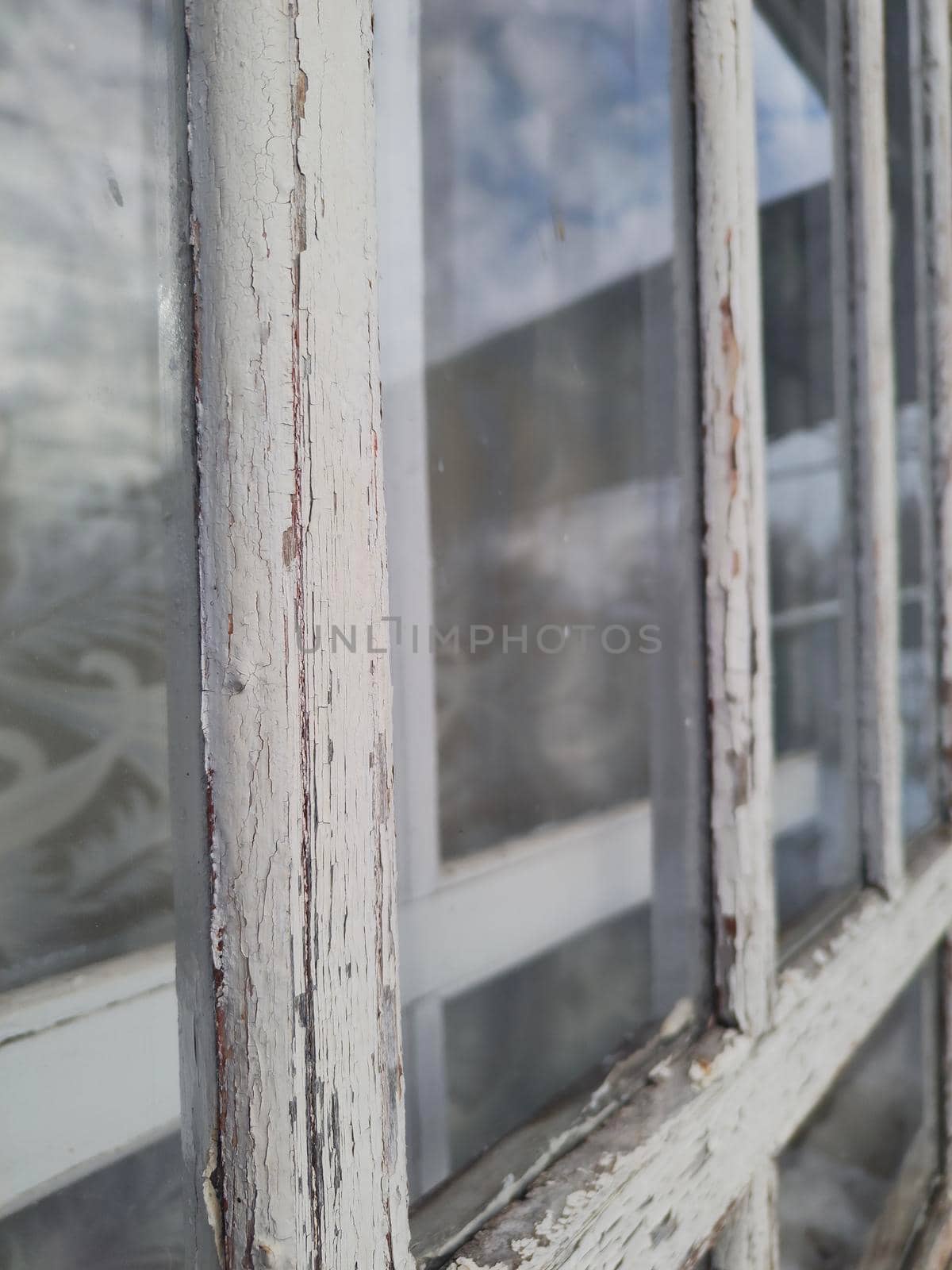 Old window with peeling white paint on the frame, focus on foreground window perspective by koksikoks