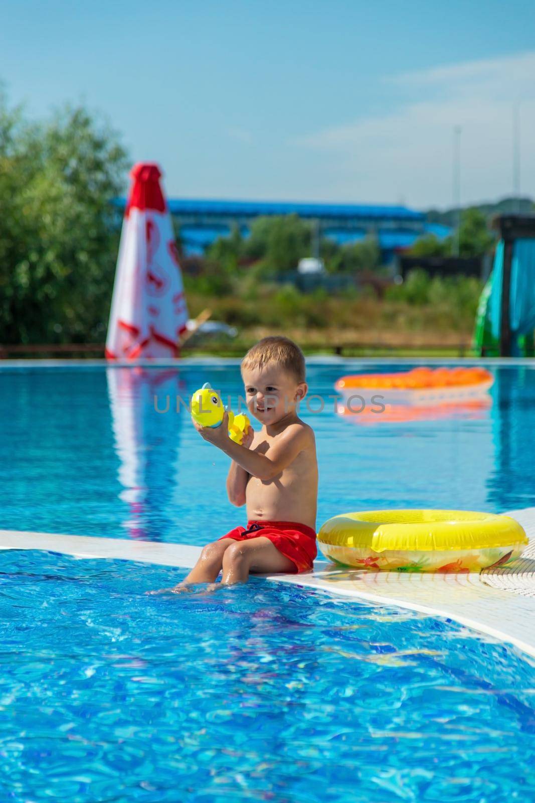 the child sits near the pool is played with a water pistol. selective focus