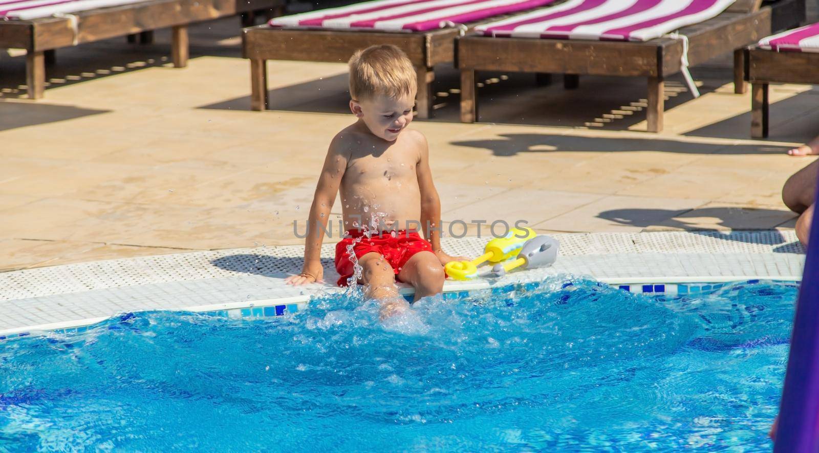 the child sits near the pool is played with a water pistol. selective focus