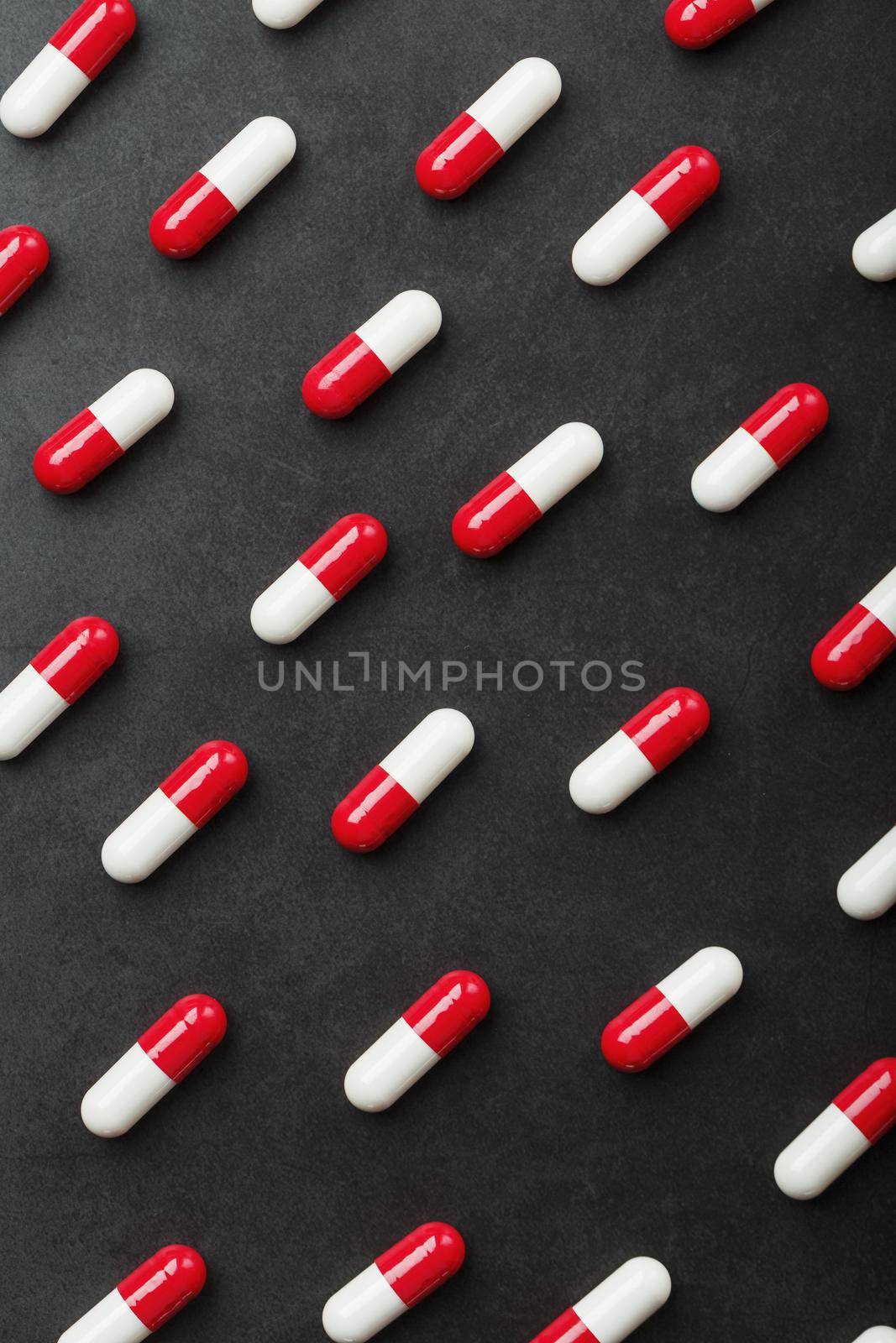 A pattern of red and white pill capsules on a black background background. by AlexGrec