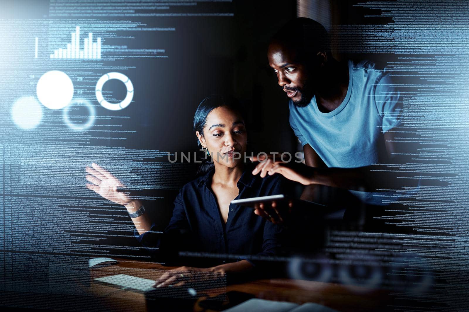 Shot of two programmers using a digital tablet while working together on a computer code at night