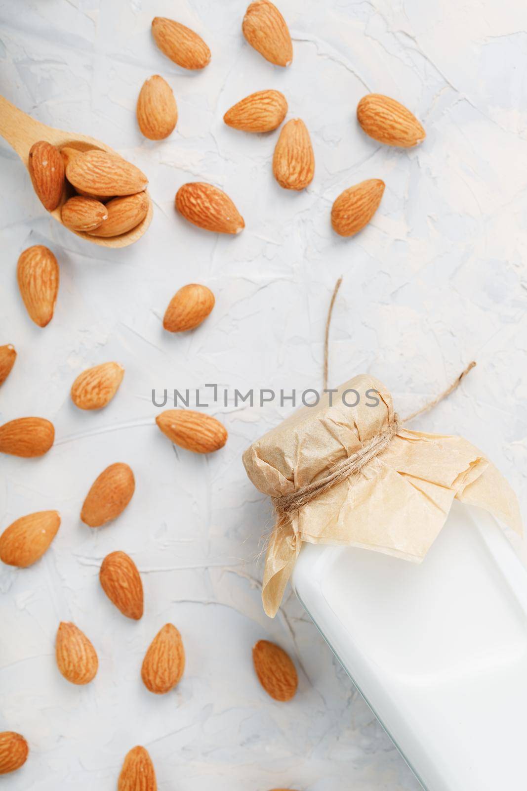 Almond milk in a glass bottle on a light background with a scattering of seed kernels and a wooden spoon. Top view