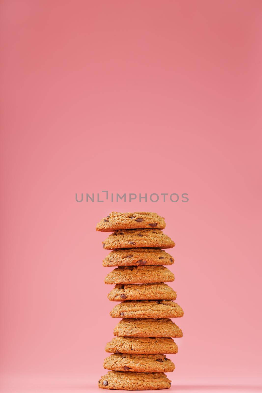 Oatmeal cookies with pieces of chocolate stand like a tower on a pink background. Minimalistic concept of Free space