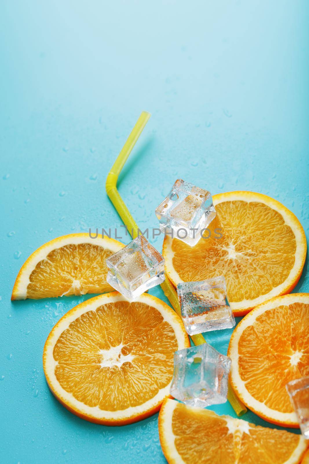 Orange slices and ice cubes with a straw on a blue background in the shape of a cocktail. The concept of the drink lemonade is a summer refreshing composition. Top view