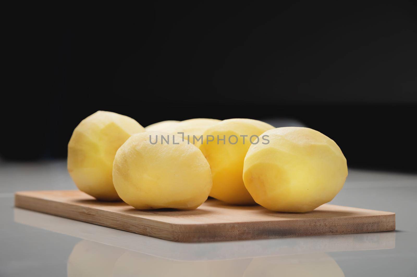 Peeled fresh potatoes on a wooden cutting board on a white table