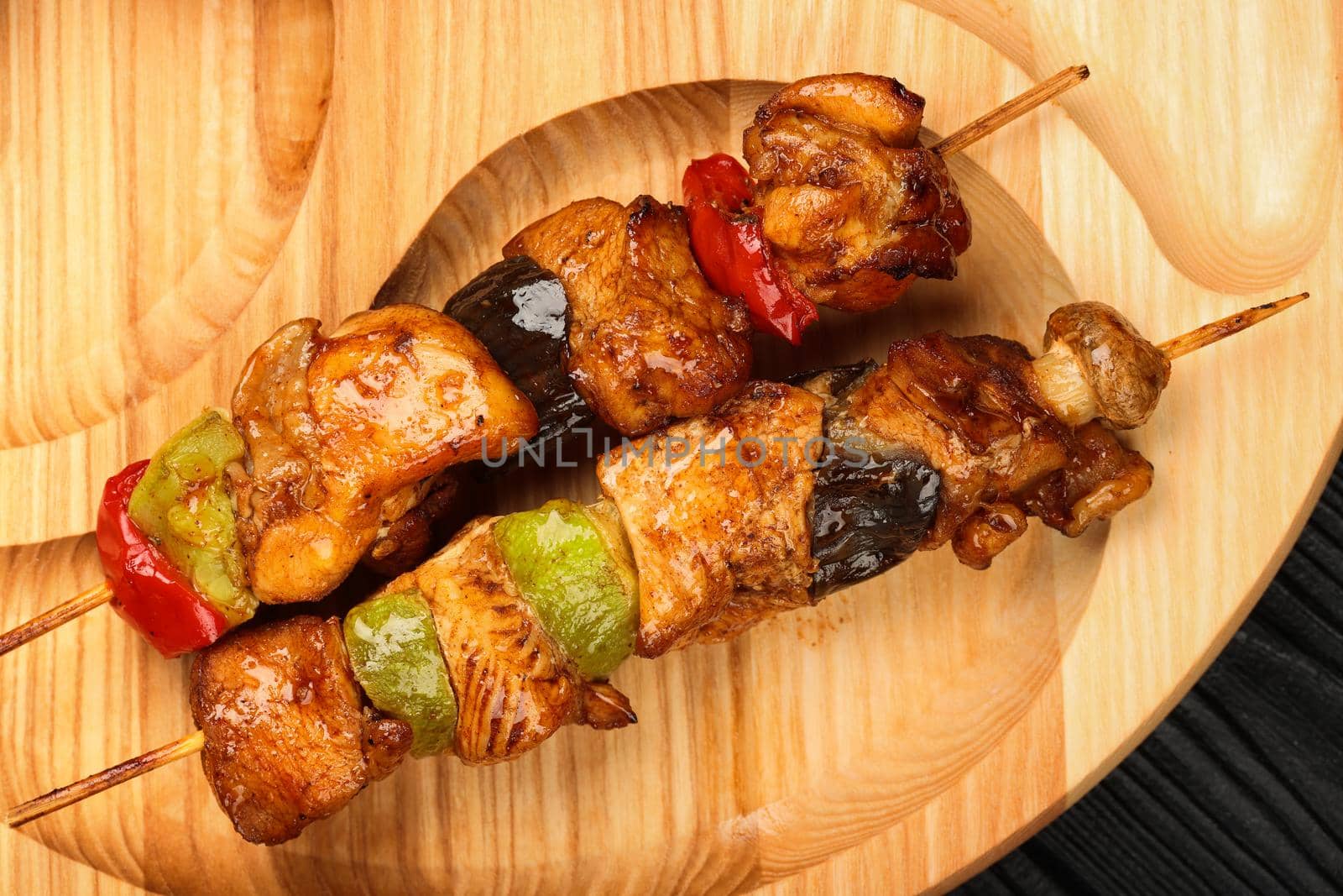 Close up portion of grilled barbecue skewed chicken meat with vegetables served on wooden board, elevated top view, directly above