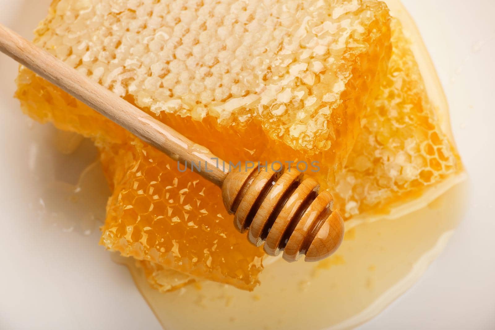 Close up stack of several fresh cut golden comb honey slices and natural wooden dipper on plate isolated on white background, top view, directly above