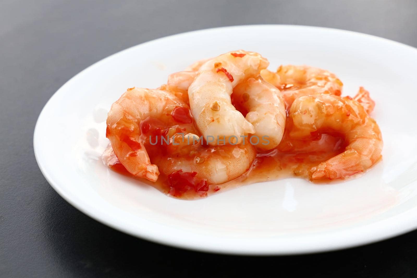 Close up portion of shrimp salad with sweet chili sauce on white plate over black table, elevated top view, directly above