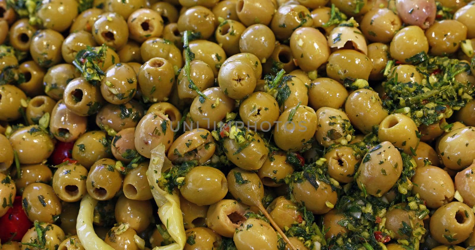 Close up background of traditional artisanal pickled green olives with spice herbs on retail display of open market, high angle view