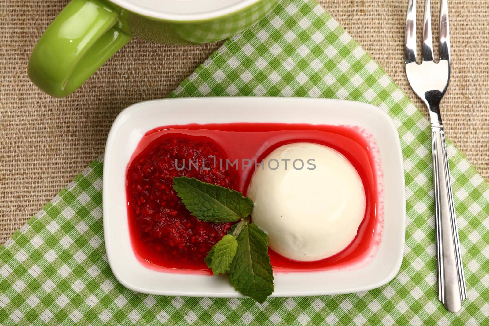 Close up serving panna cotta traditional Italian dessert with raspberry jam and cup of hot drink, elevated top view, directly above