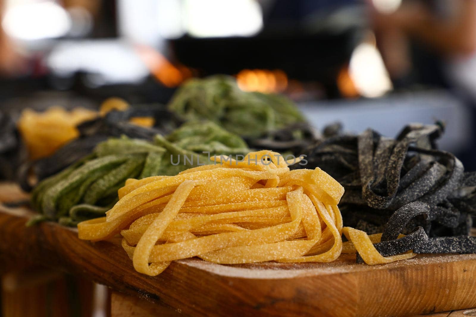 Close up cooking fresh handmade traditional Italian tagliatelle pasta, uncooked black, green and classical past on wooden table, high angle view